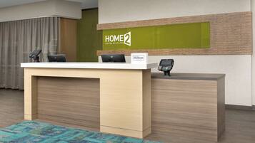 A reception desk with a sign reading "HOME 2 Suites by Hilton" and a nameplate that says "Hilton Honors".