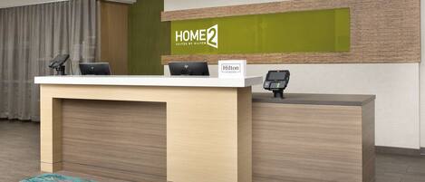 A reception desk with a sign reading "HOME 2 Suites by Hilton" and a nameplate that says "Hilton Honors".
