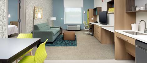 A modern hotel room with a dining area, kitchenette, and a large window.