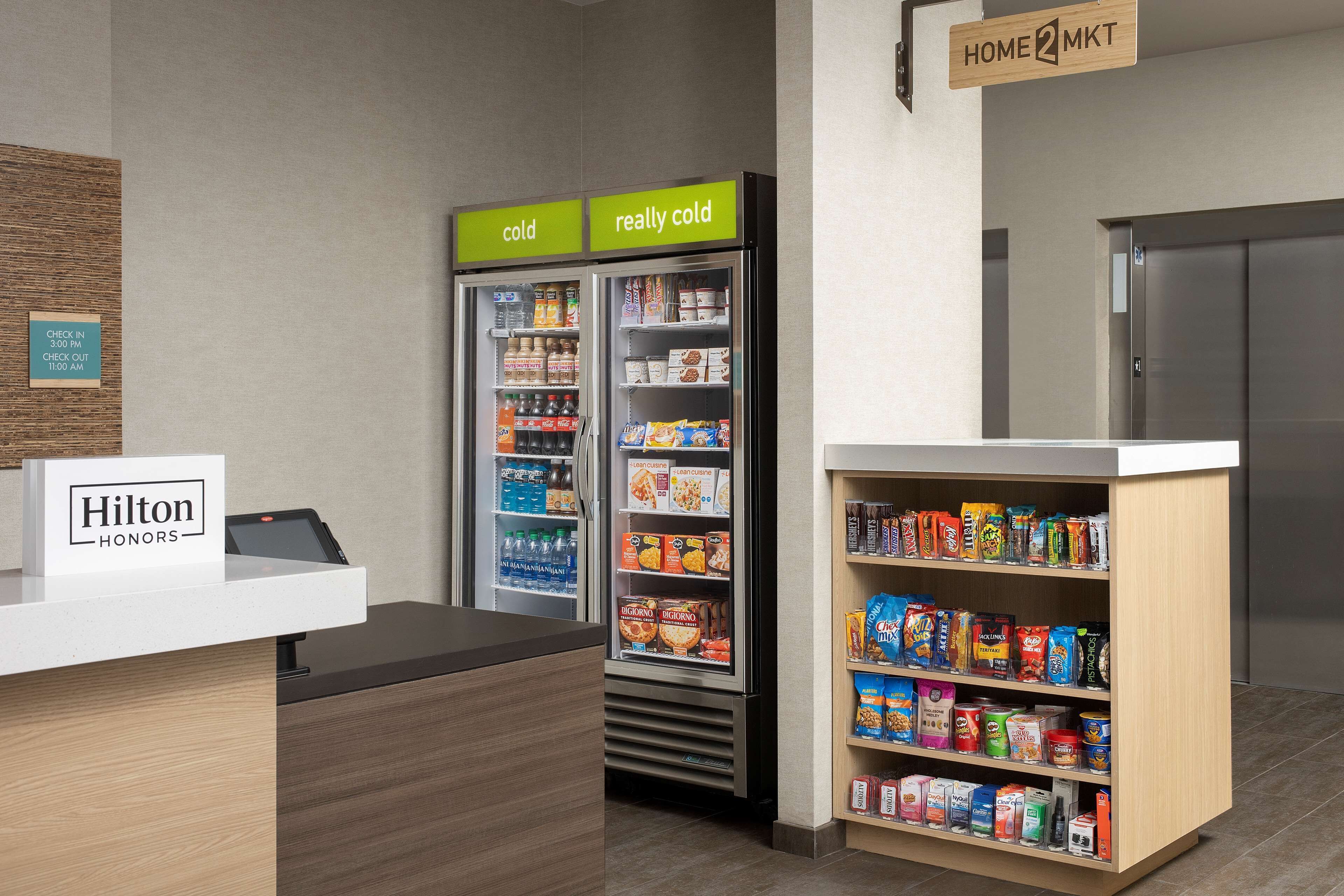 A hotel reception area with a minibar, a self-service snack station, and a sign indicating the location of the home and minibar.