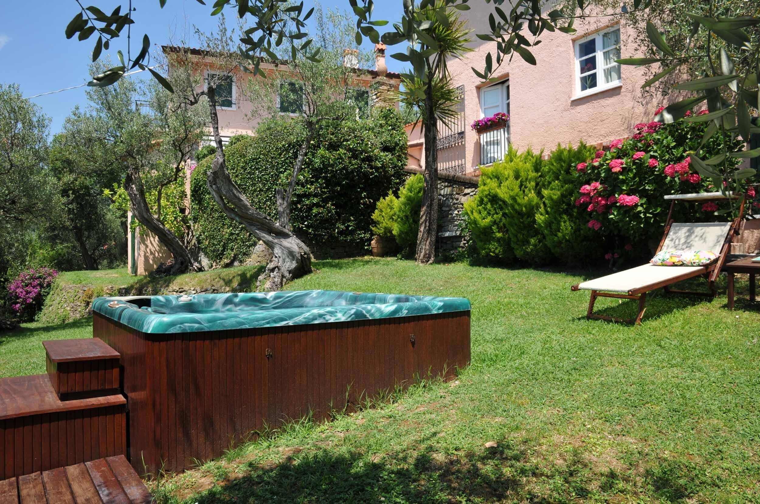 Een achtertuin met een jacuzzi, een houten terras en een ligstoel.