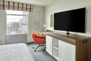 A hotel room with a bed, a desk with a computer, a TV, and a window with a city view.