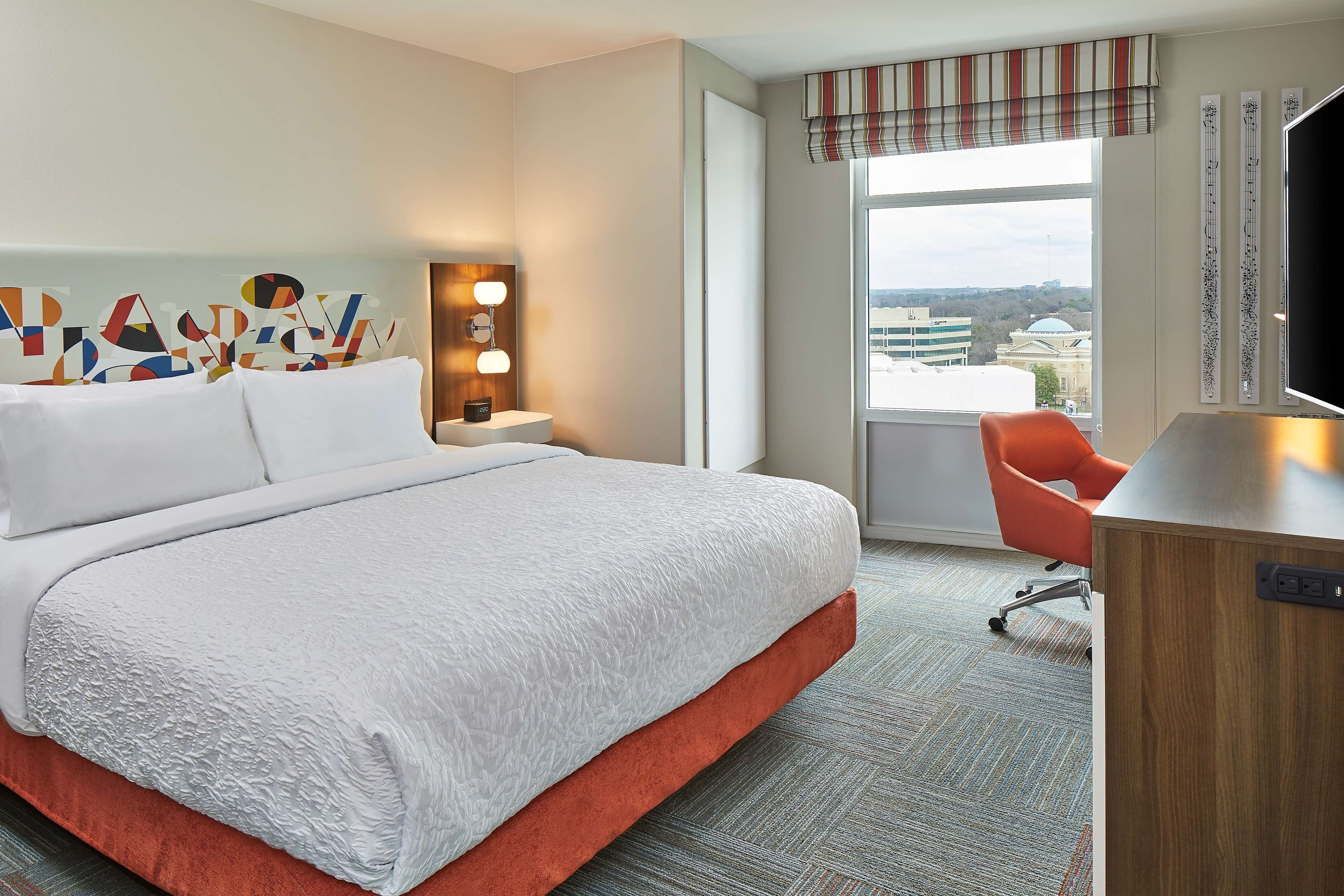 A hotel room with a large bed, a desk, a chair, a window with a view, and a wall with decorative elements.