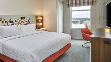 Habitación de hotel con una cama grande, un escritorio, una silla, una ventana con vistas y una pared con detalles decorativos.