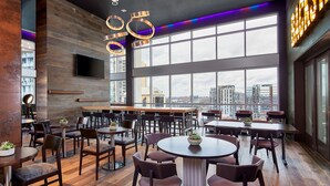 Een modern restaurant met hoge plafonds, grote ramen en uitzicht over de stad.