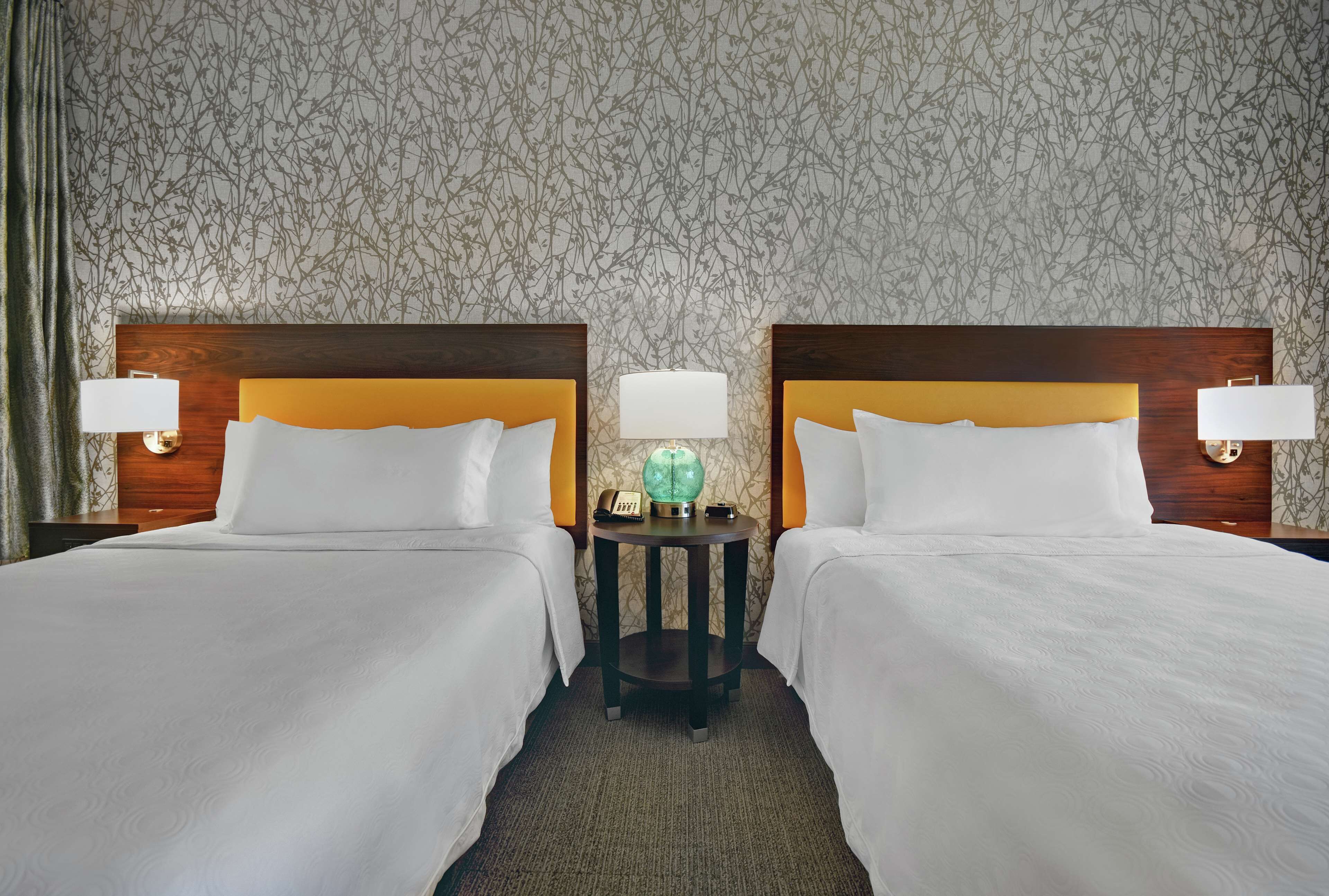 A hotel room with two beds, a round table with a globe, and lamps on either side.
