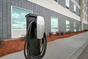 A Tesla charging station in front of a modern building with large windows and a brick facade.