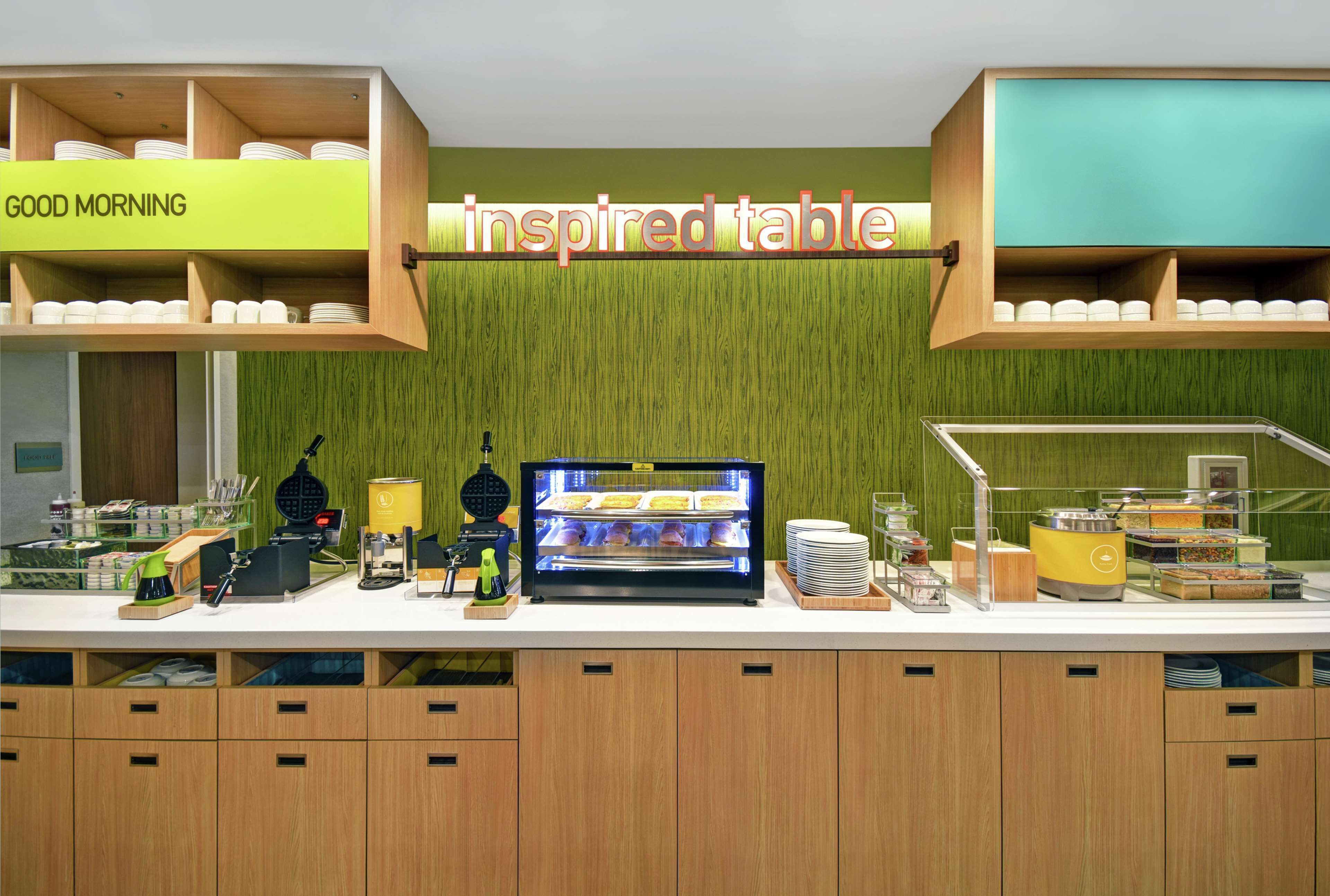 A breakfast bar with a 'Good Morning' sign, a self-service station with a variety of food items, and a 'Inspired Table' sign.