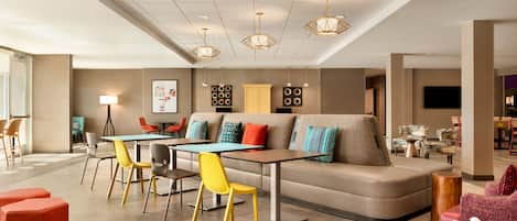 A modern lounge area with a sofa, tables, chairs, and a flat-screen TV.