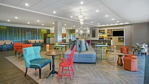 A modern hotel lobby with a variety of seating options, a reception desk, and a kitchenette area. - Home2 Suites by Hilton Lawrenceville Atlanta Sugarloaf, GA (Lawrenceville)