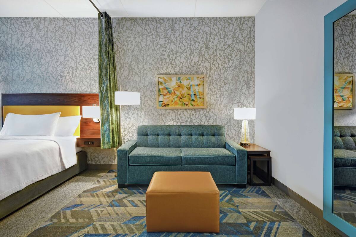 Ein Hotelzimmer mit einem Bett, einer Couch, einem kleinen Tisch und einem Spiegel.