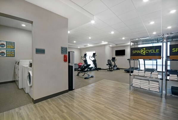 Un gimnasio de hotel con equipo de ejercicio, zona de lavandería y un letrero de Spin2Cycle.