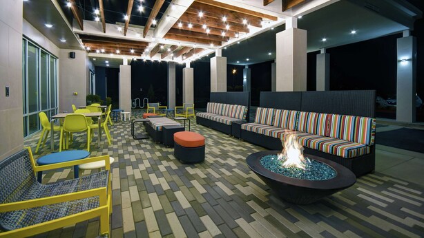 An outdoor patio area with seating, a fire pit, and a ceiling with exposed beams and string lights. - Home2 Suites by Hilton Lawrenceville Atlanta Sugarloaf, GA (Lawrenceville)