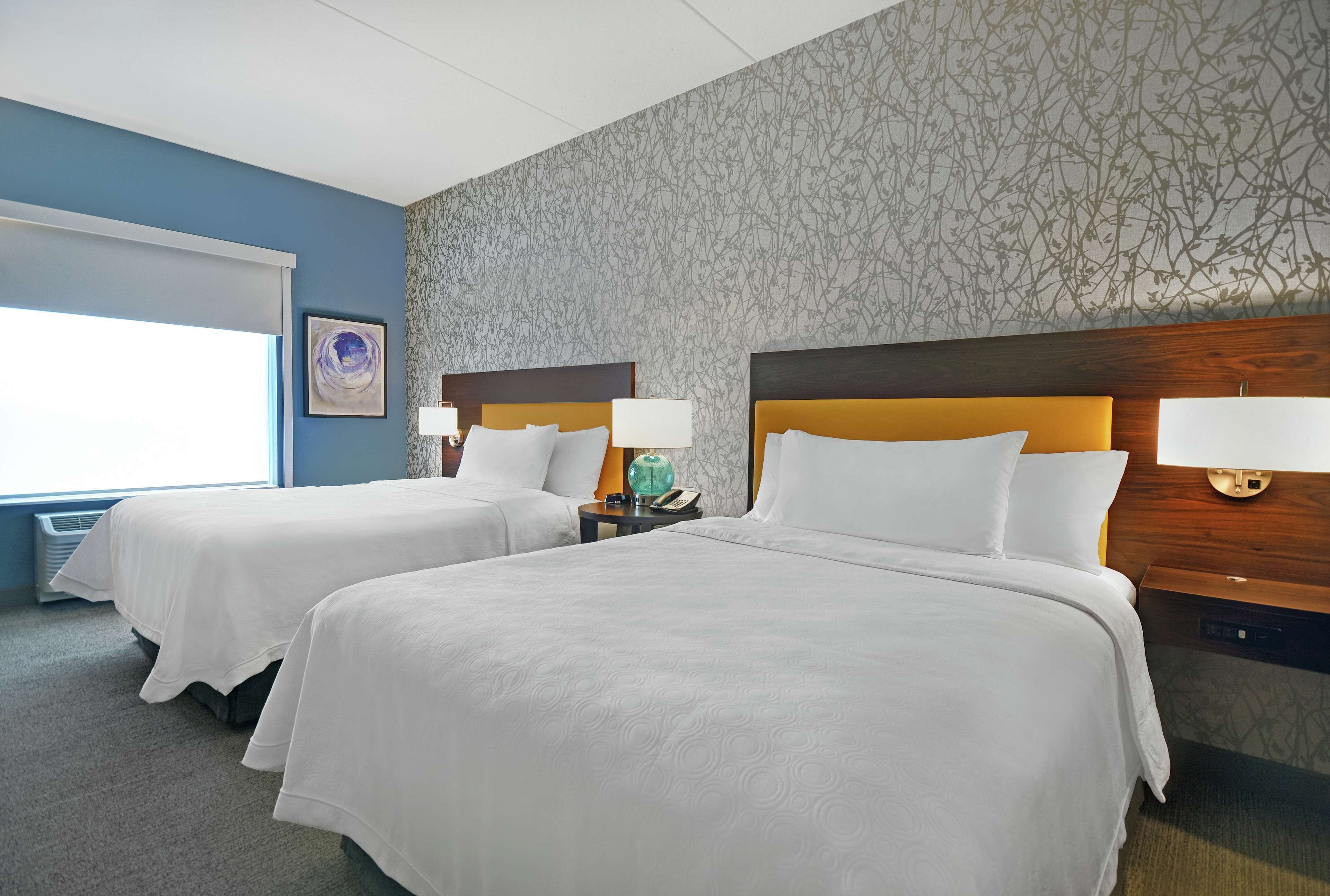 Ett hotellrum med två sängar, ett stort fönster och en vägg med ett mönster.