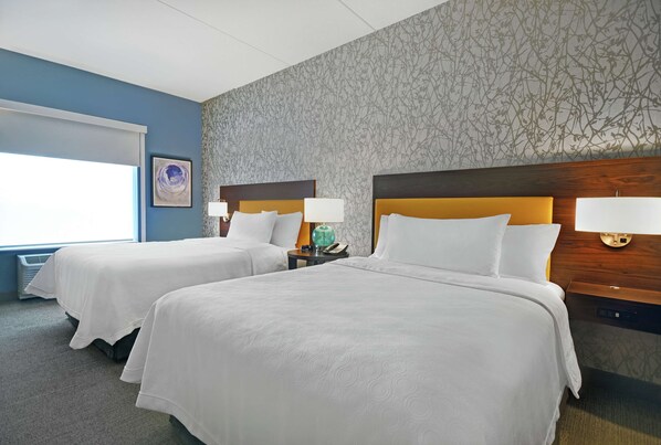 Habitación de hotel con dos camas, un ventanal grande y un papel tapiz estampado.