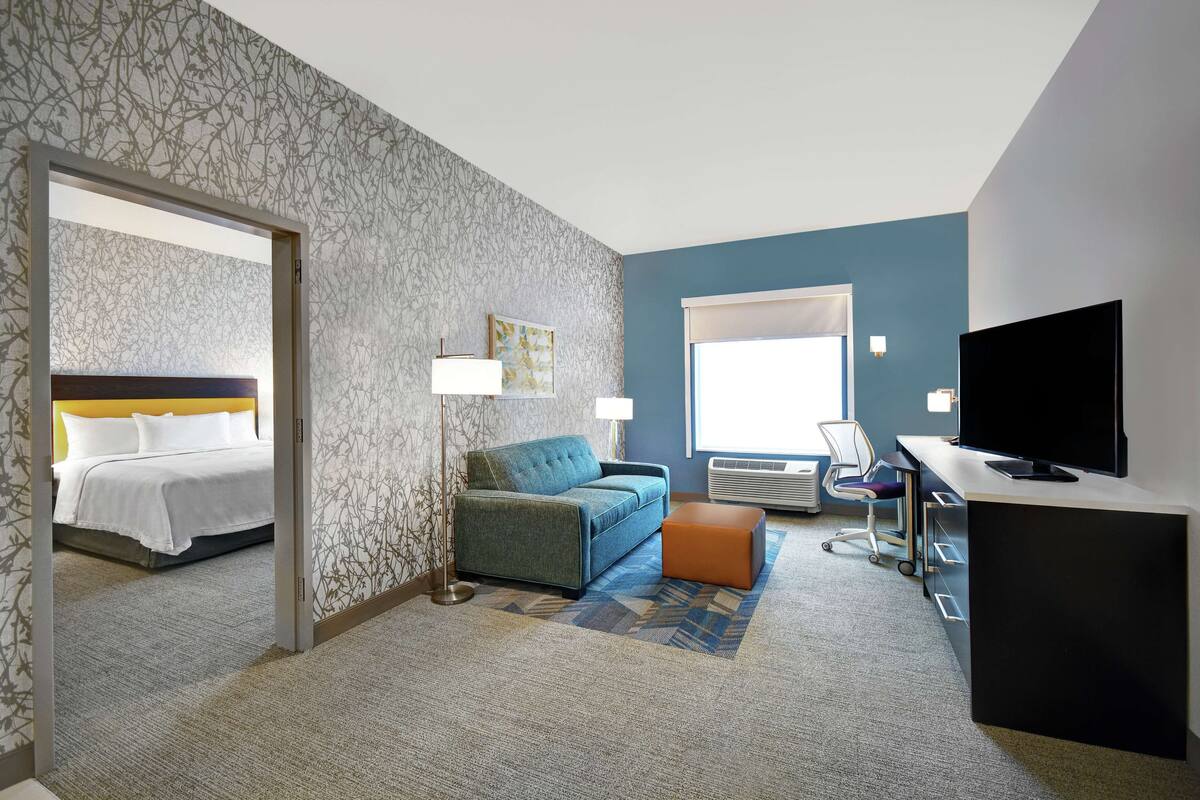 Ein Hotelzimmer mit einem Bett, einem Sofa, einem Schreibtisch mit Fernseher und einem Fenster.