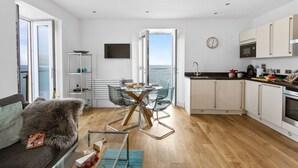 A modern kitchen with a view of the sea, a dining area with a glass table, and a cozy seating area with a fur throw.