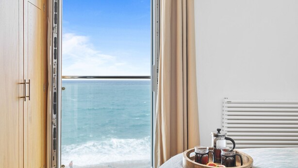 A room with a large window overlooking the sea, a wooden wardrobe, and a tray with a coffee maker and cups.