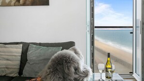 A room with a view of the beach, a bottle of wine, and two glasses on a table.