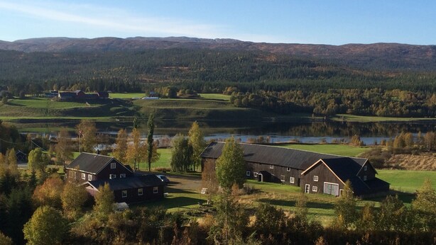 A rural landscape with a large barn and a smaller house, surrounded by trees and a lake. - Four Bedroom Guesthouse in Fjerdingen, Harran (Fjerdingen)