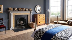 A bedroom with a fireplace, a wooden dresser, a bed with patterned bedding, and large windows. - A fusion of Georgian and Modern. Impeccably furnished with excellent attention to detail! (Edinburgh)
