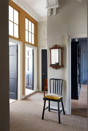 Enter a spacious entryway with a high ceiling and large window, featuring a comfortable chair and mirror.