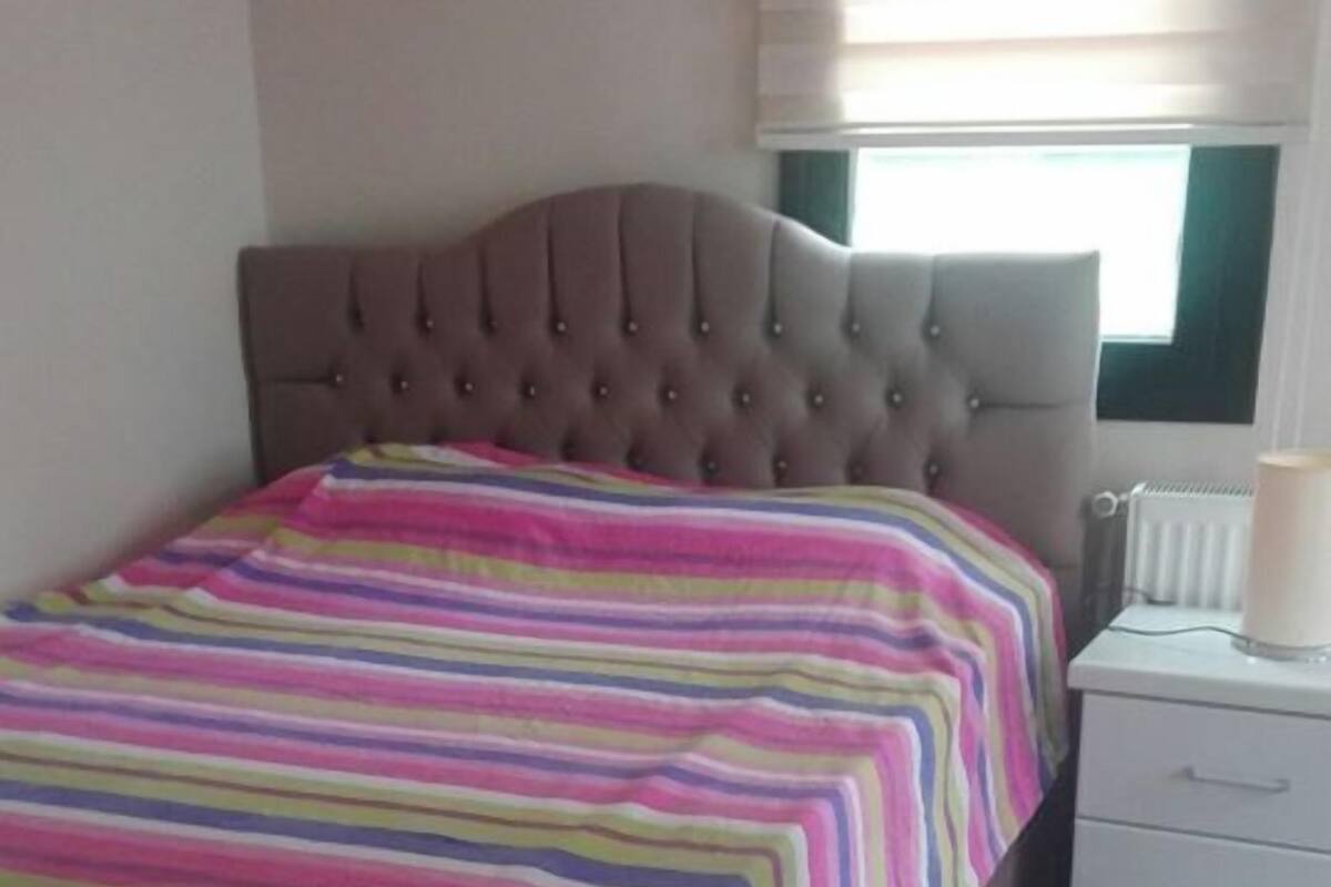A bedroom with a bed, a nightstand, and a window with blinds.