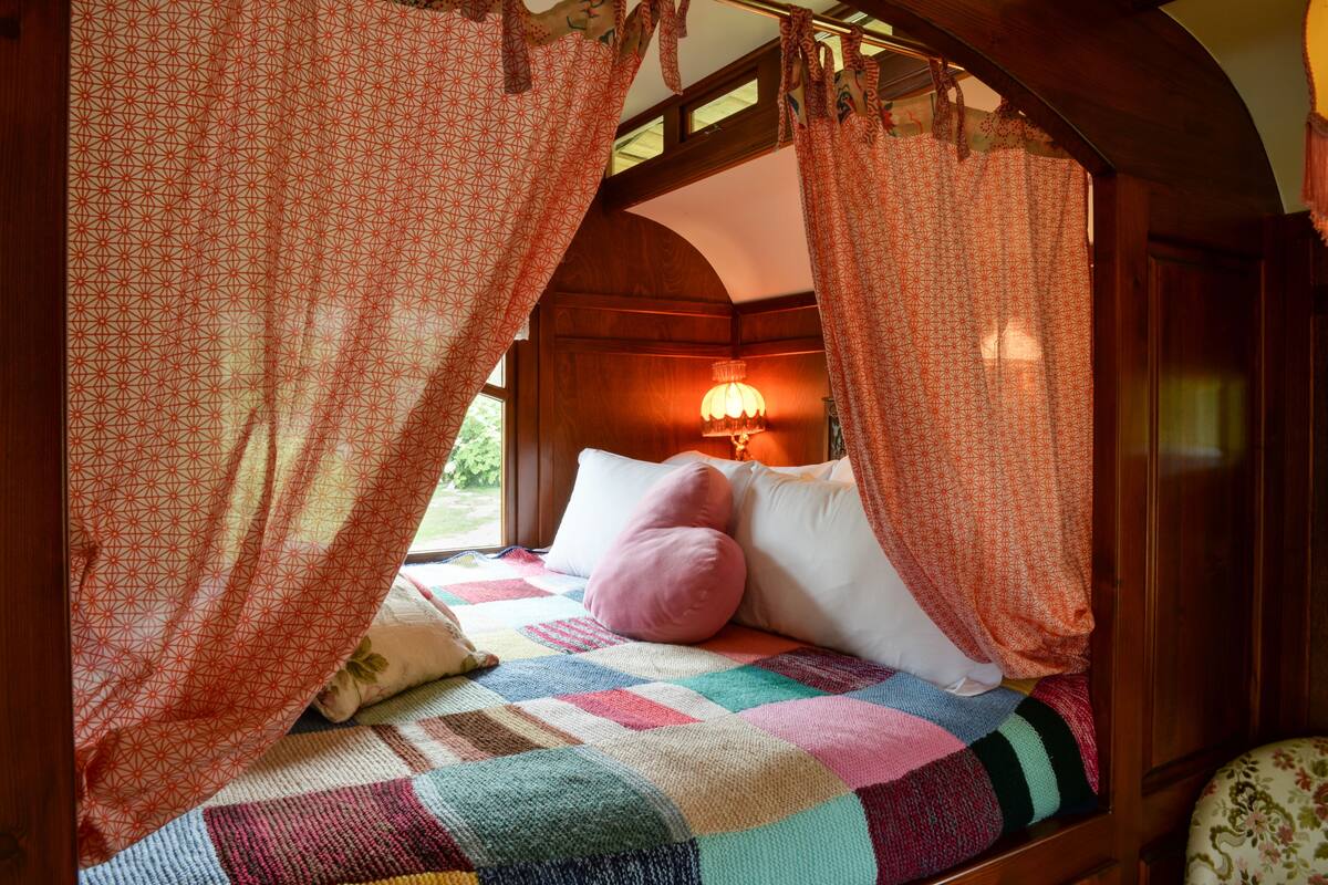 A cozy bed with a colorful quilt, a pink pillow, and a lamp in the background.
