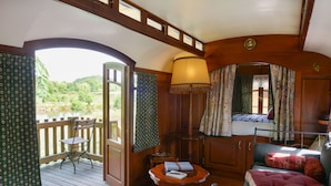 A cozy cabin with a wooden deck, a small table with a lamp, a bed with patterned curtains, and a view of the outdoors. - La Maison de Mezos (Mézos)