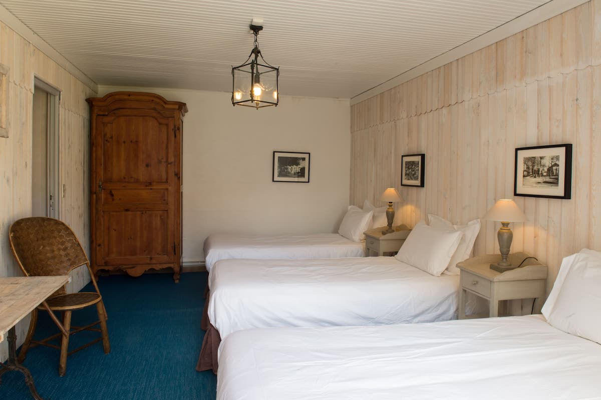 A hotel room with two single beds, a wooden wardrobe, a desk with a chair, and a ceiling light fixture.