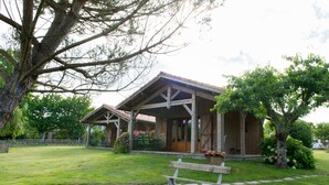 A rustic wooden building with a covered porch and a grassy lawn. - La Maison de Mezos (Mézos)