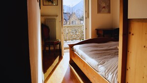 A bedroom with a wooden bed, a chair, a radiator, and a window with a view of mountains. - Central, spacious and comfortable, easy to reach by car or train. (Merano)