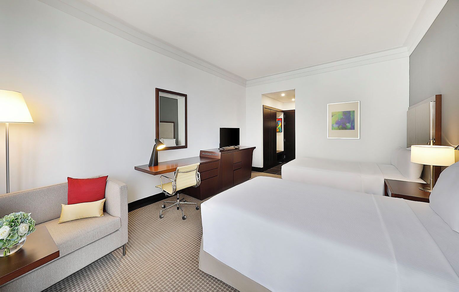 A hotel room with a bed, a desk with a chair, a dresser, a sofa, and a lamp.