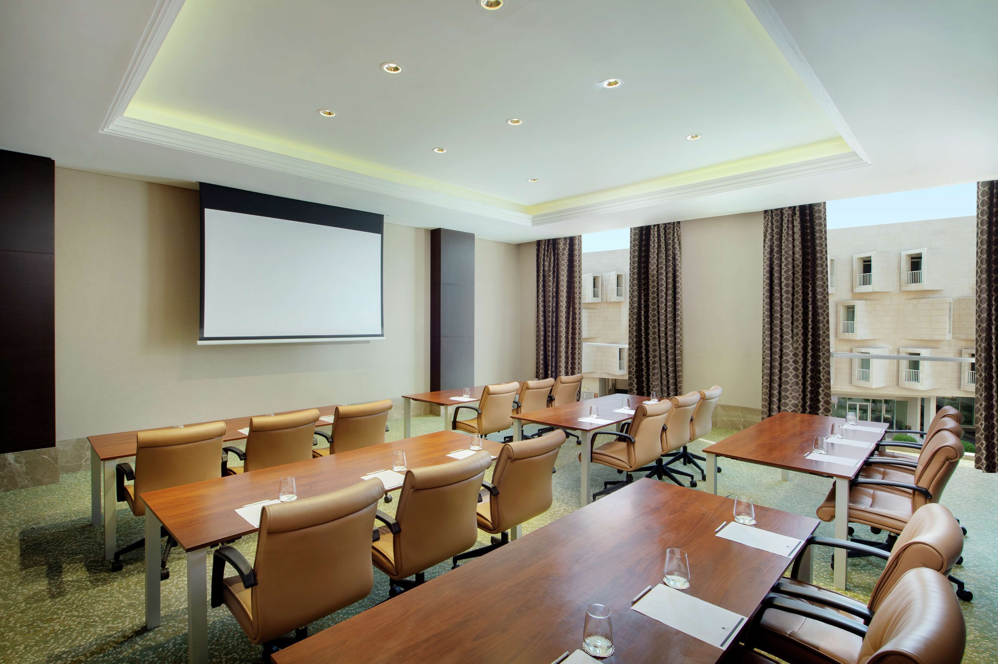 A conference room with a large screen, multiple tables, and chairs.