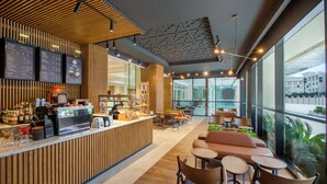 A modern cafe with a wooden counter, seating area, and large windows. - DoubleTree by Hilton Doha - Al Sadd (Doha)
