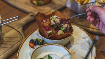 A bowl of food with a spoon, a plate with a fork, and a basket of fries in the background.