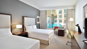 A hotel room with two beds, a desk, a chair, a TV, and a view of a swimming pool.