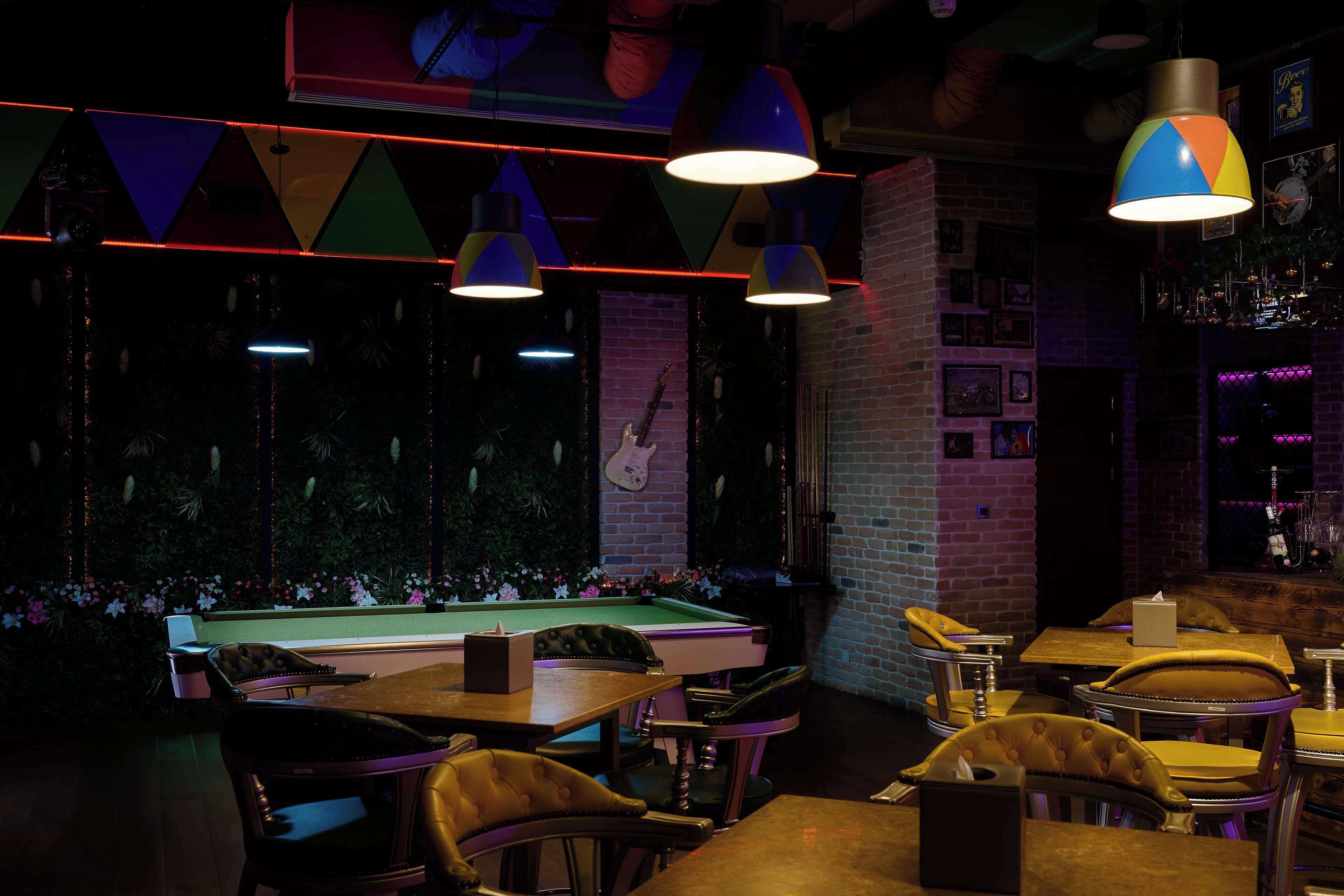 A bar area with pool tables, leather chairs, and hanging lamps.