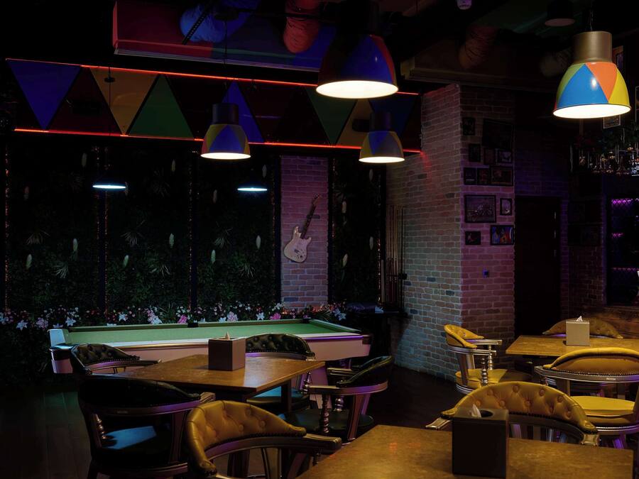 A bar area with pool tables, leather chairs, and hanging lamps.