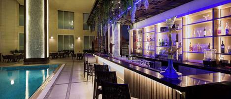 A bar area with a pool, bar stools, and shelves of bottles.
