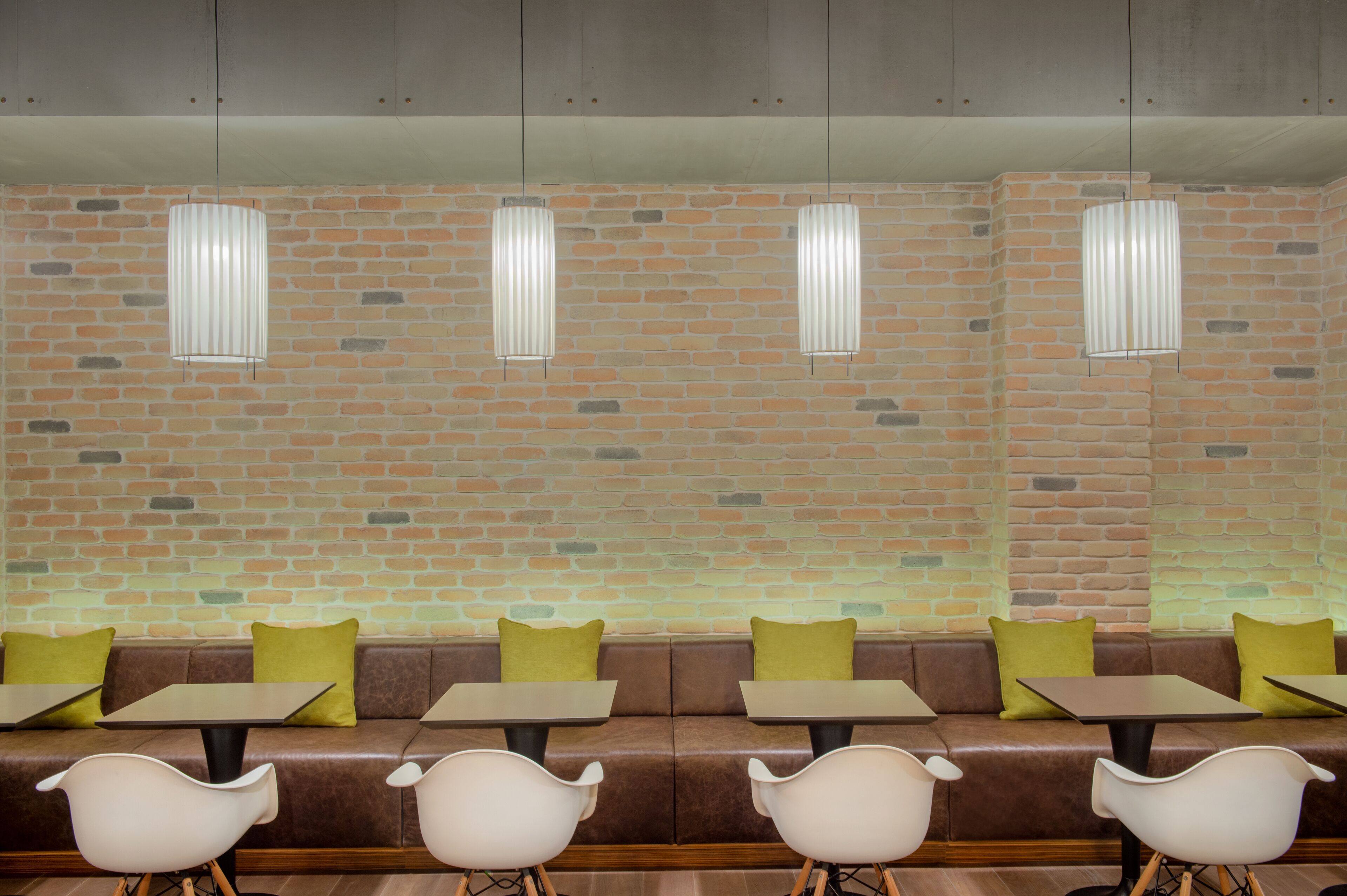 A seating area with a brick wall, cushioned benches, and tables.