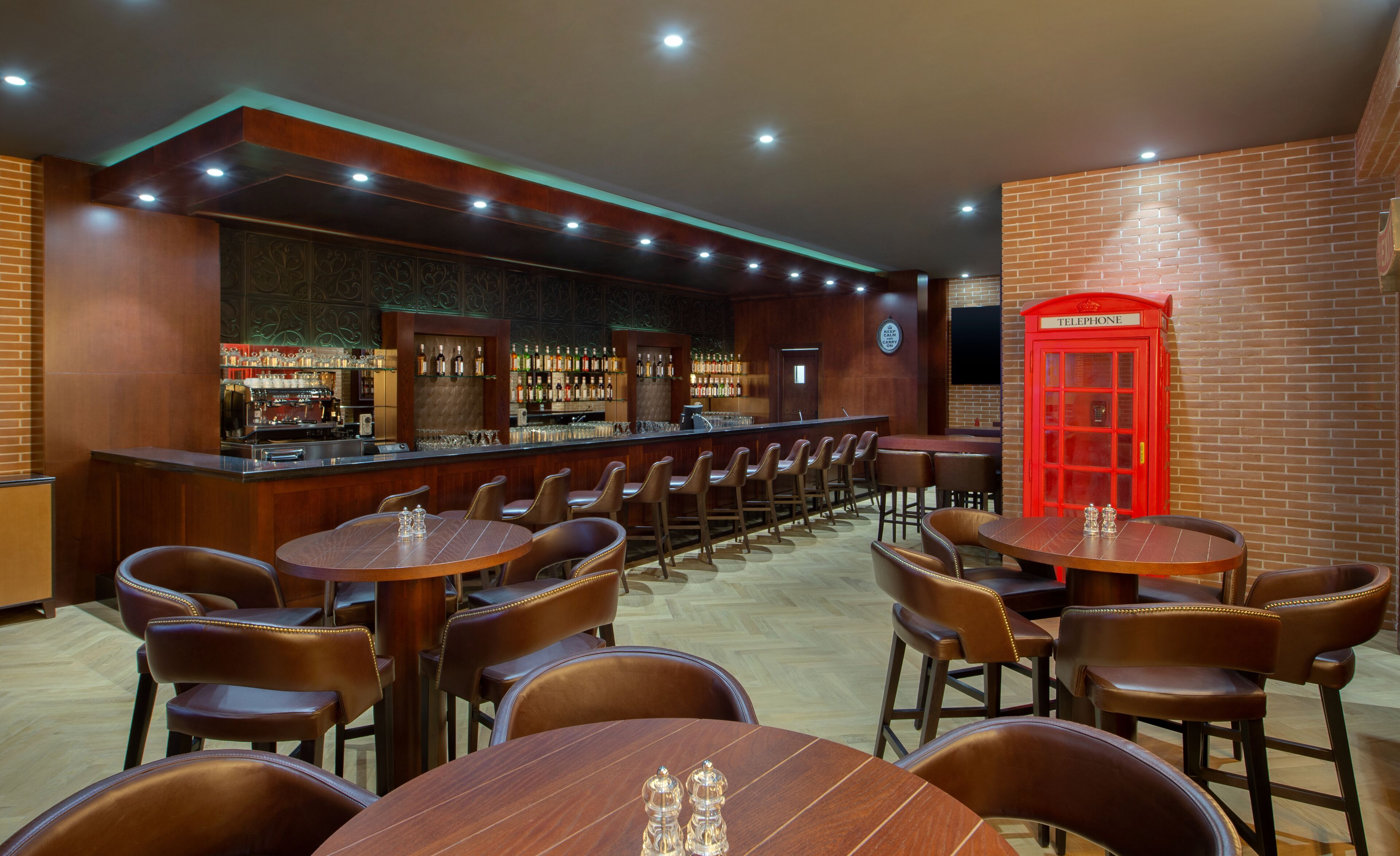A bar area with wooden tables and chairs, a red telephone booth, and a brick wall.