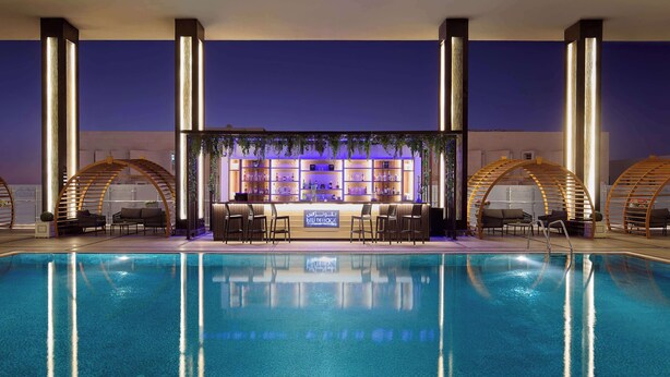 A poolside bar area with seating and a sign indicating a minibar service. - DoubleTree by Hilton Doha - Al Sadd (Doha)