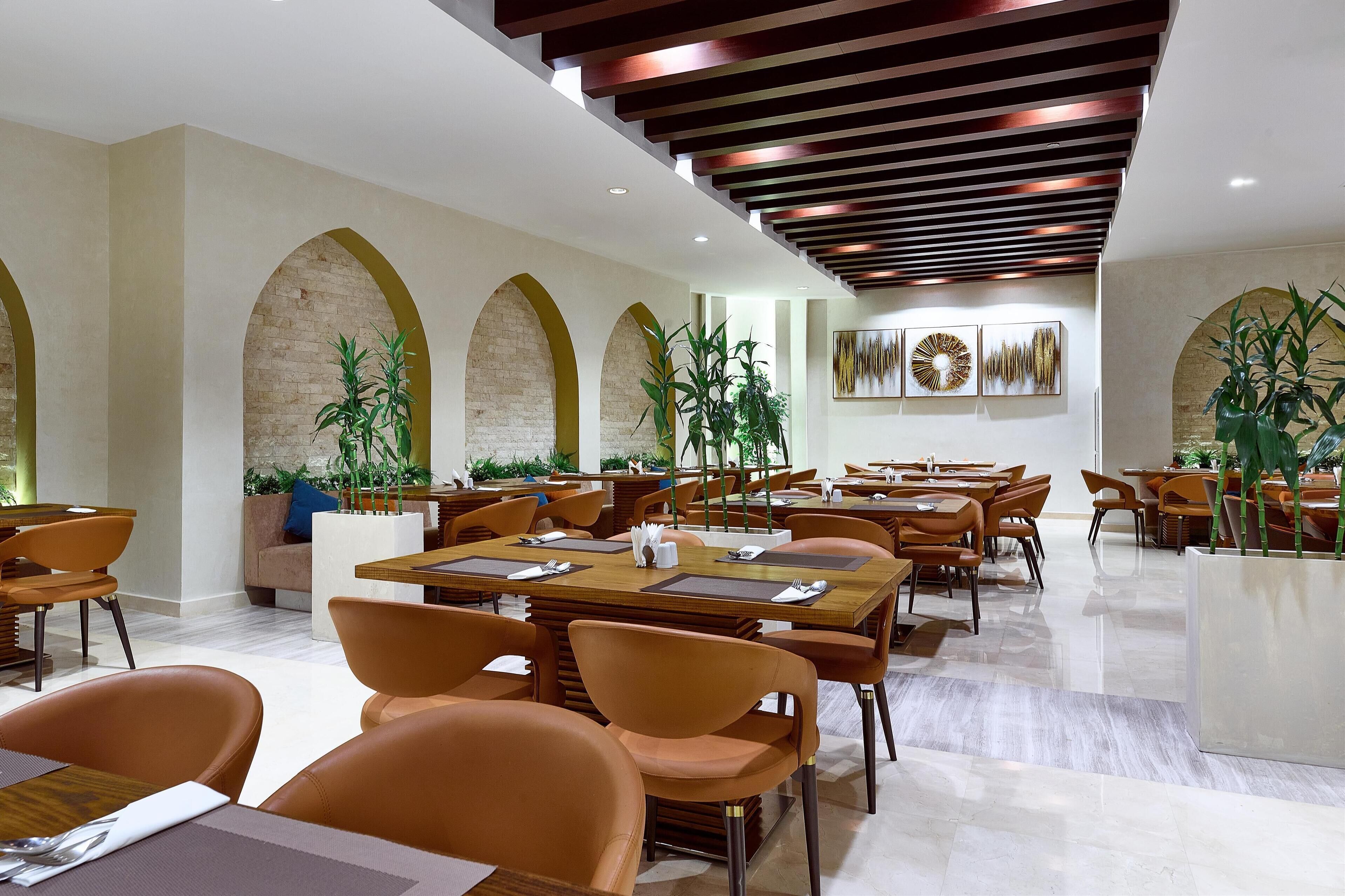 Un comedor amplio con varias mesas y sillas, que destaca por un diseño moderno del techo y arcos de ladrillo.