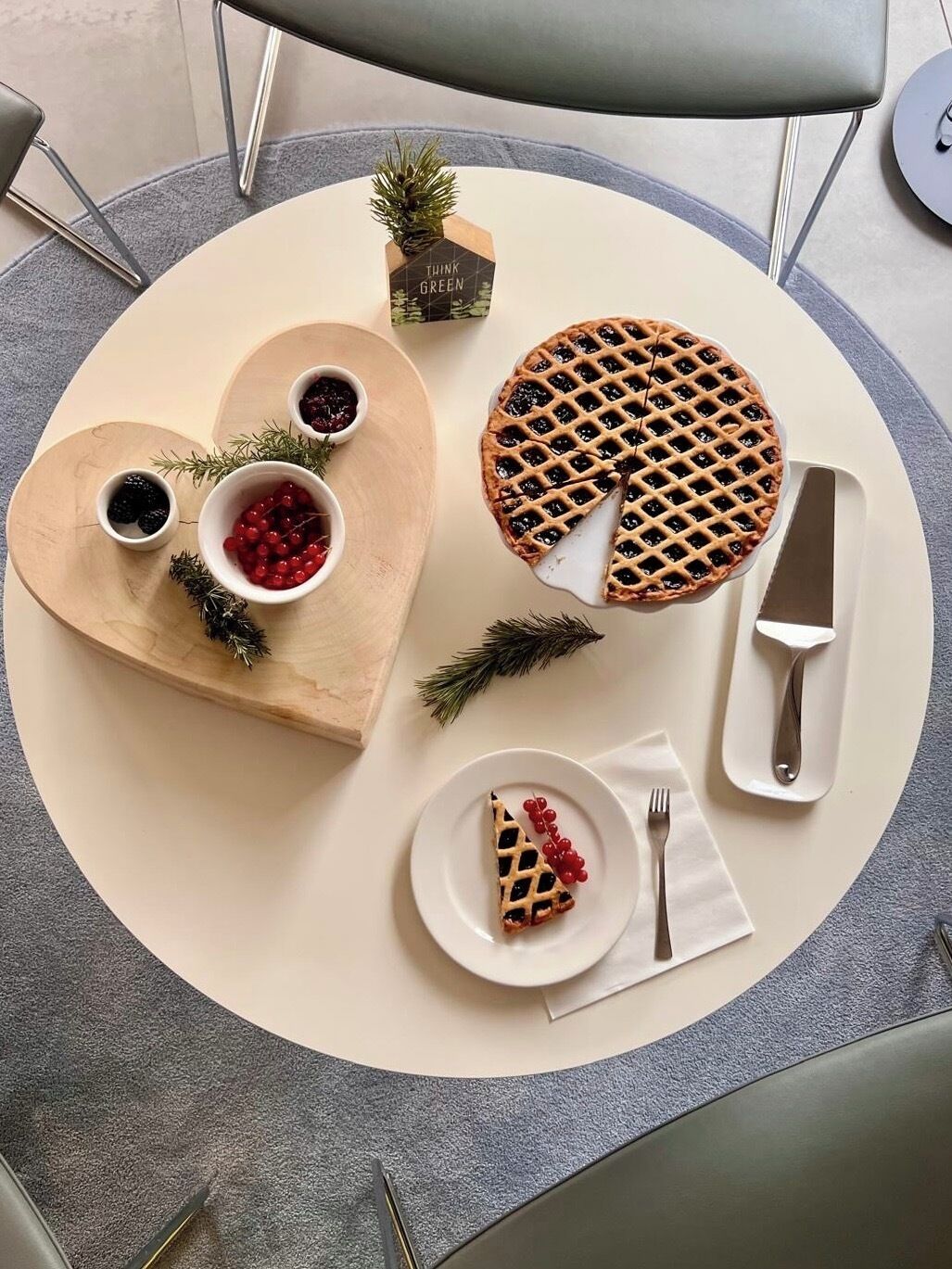 Une table sur laquelle se trouve une planche de service en forme de cœur, avec des baies et une tarte, une petite plante, ainsi qu’un couteau et une fourchette.