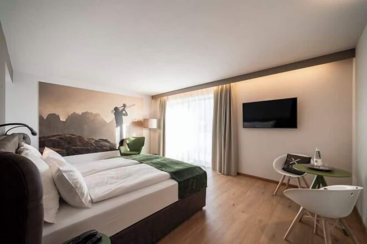Une chambre d’hôtel avec un lit, une télévision, un bureau avec une chaise et un tableau au mur.