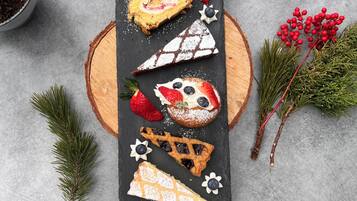 Une variété de pâtisseries et de desserts disposés sur une ardoise, accompagnés de fraises et de myrtilles fraîches, ainsi que de quelques éléments de décoration végétale.