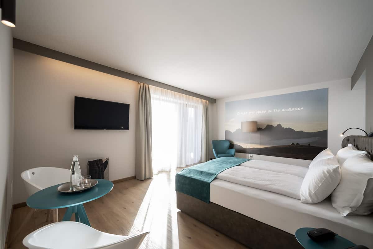 Une chambre d’hôtel moderne équipée d’un lit, d’un bureau, d’une chaise, d’une télévision et d’une fenêtre avec des rideaux.