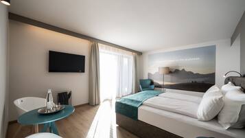 A modern hotel room with a bed, a desk, a chair, a TV, and a window with curtains.