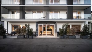 A modern hotel with a double-height entrance, large windows, and outdoor seating. - Be Place (Trento)